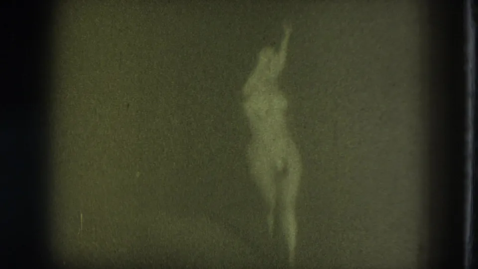 1975 San Francisco 8mm frame showing an adult woman wearing pasties, softly focused as she dances against a dark backdrop.