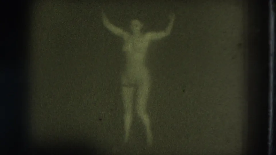 1975 San Francisco 8mm frame of an adult woman wearing pasties with both arms raised while dancing in low light.