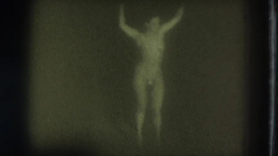 1975 San Francisco 8mm frame showing an adult woman in pasties dancing with raised arms, blurred by motion and soft focus.