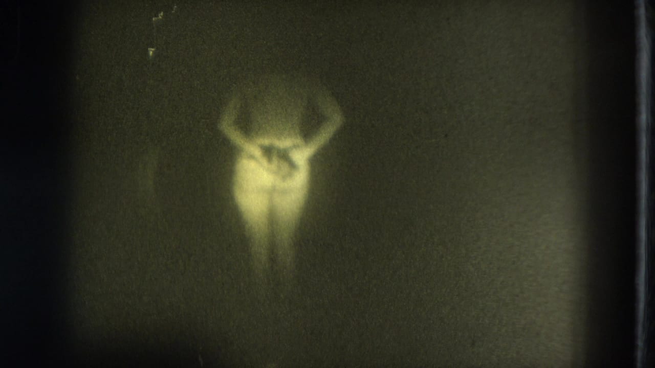1975 San Francisco 8mm frame showing a soft, green-tinted silhouette of a woman with arms raised in low light.