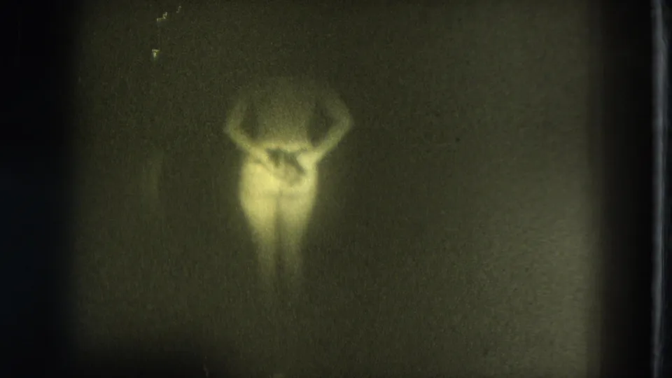 1975 San Francisco 8mm frame showing a soft, green-tinted silhouette of a woman with arms raised in low light.