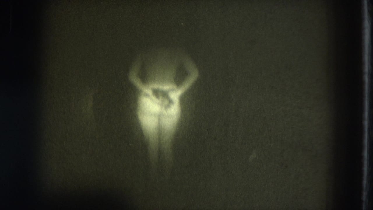 1975 San Francisco 8mm frame with a woman in soft silhouette, arms raised, seen through grain and underexposure.