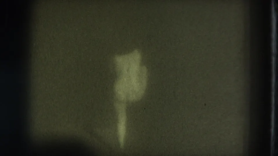 1975 San Francisco Super 8 frame showing a distant nude adult woman on a dark stage in low green-yellow light.