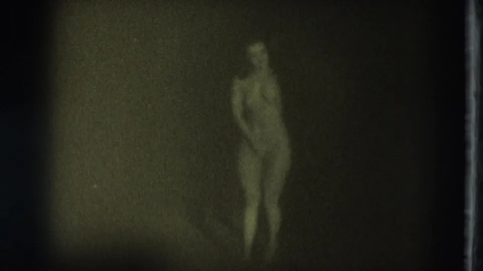 1975 San Francisco Super 8 frame of a nude adult woman standing in dim light, with facial detail faint and indistinct.
