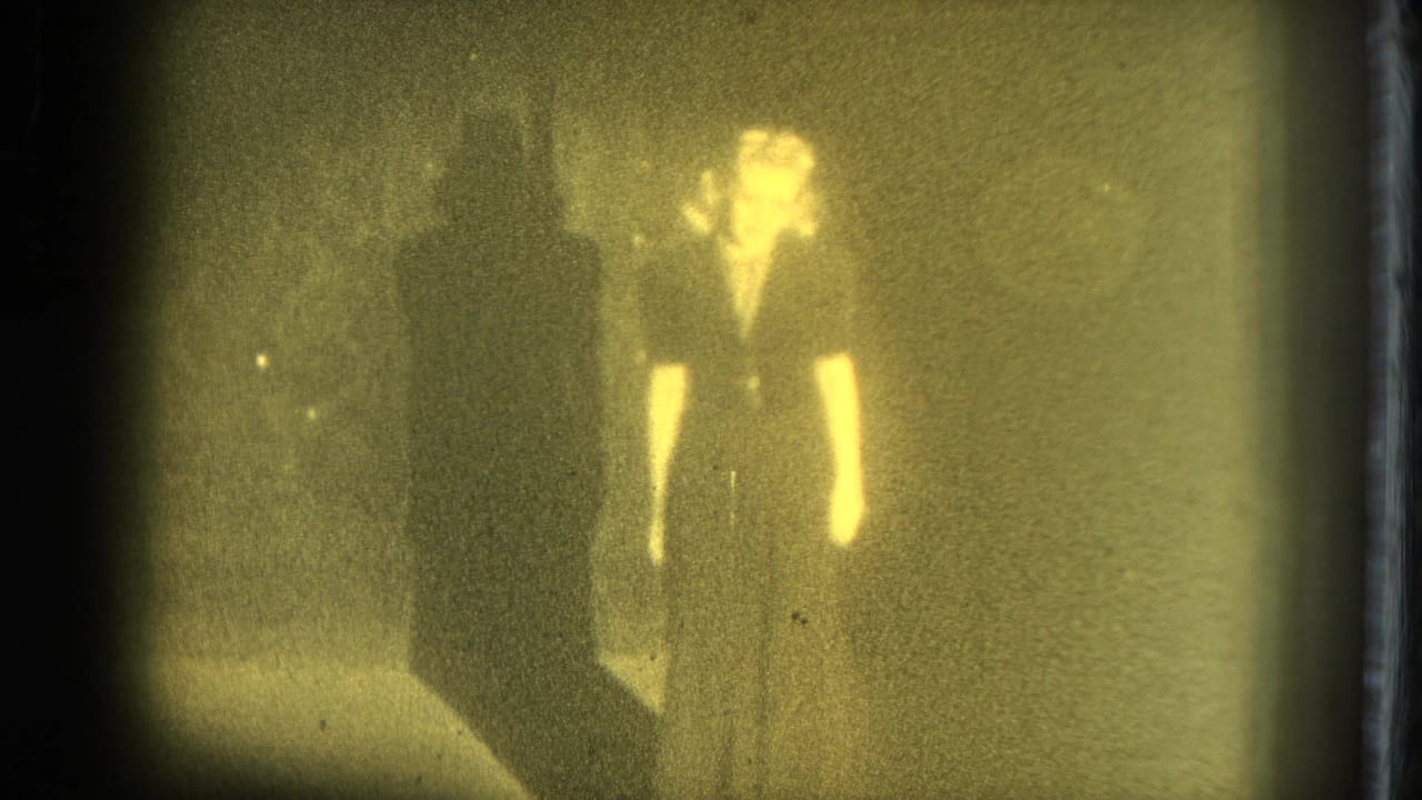 Adult woman faces forward in a dark outfit under dim yellow lighting.