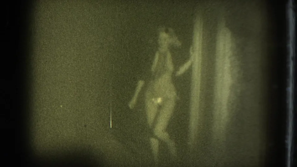 1975 San Francisco 8mm frame showing an adult woman in a revealing costume posing near curtains during a dim indoor performance.
