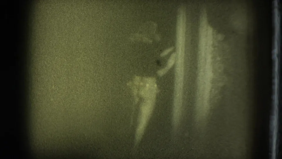 Soft 8mm frame of a female performer on a dark stage in the 1975 San Francisco clip, partly obscured by low light and film blur.