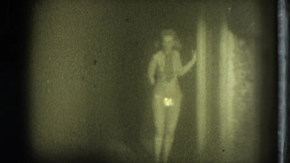 Female performer stands near a bright vertical stage edge in the 1975 San Francisco home-movie clip, with soft focus and visible film grain.