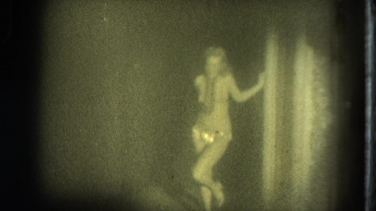 Woman in a light outfit poses near a curtain in a dim, grainy room.