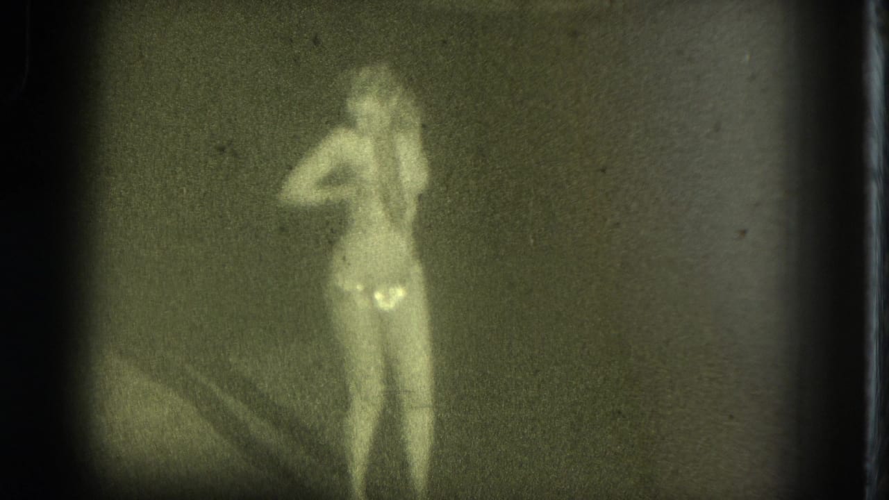 Female performer standing in a dim green-tinted frame with one hand near her head.
