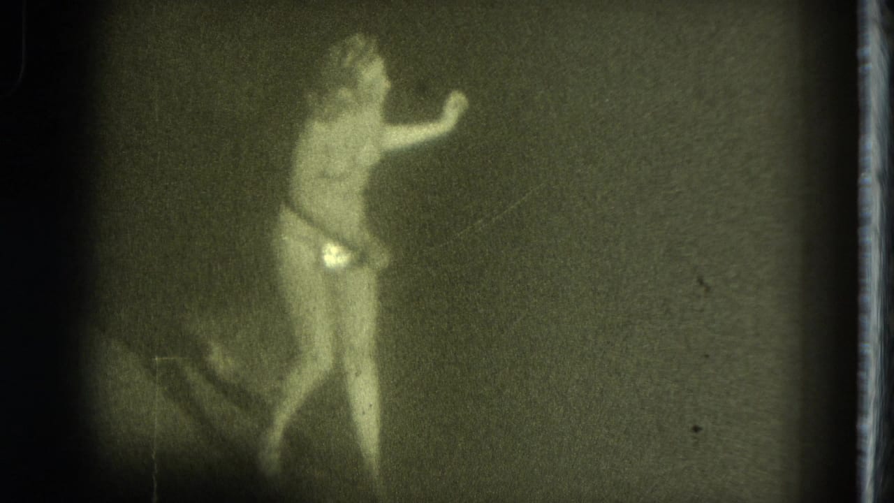 A dancer or entertainer appears in a dim 1975 San Francisco frame, with one arm extended and reflective costume details visible.