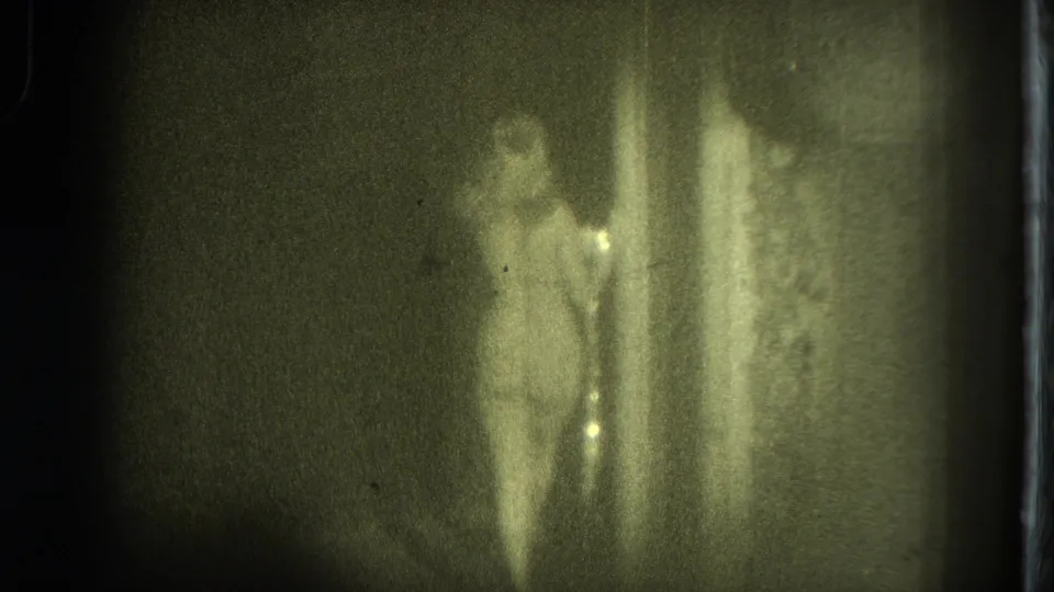 A distant performer is partly obscured by dim exposure and a vertical edge, with 8mm grain and green tint prominent.