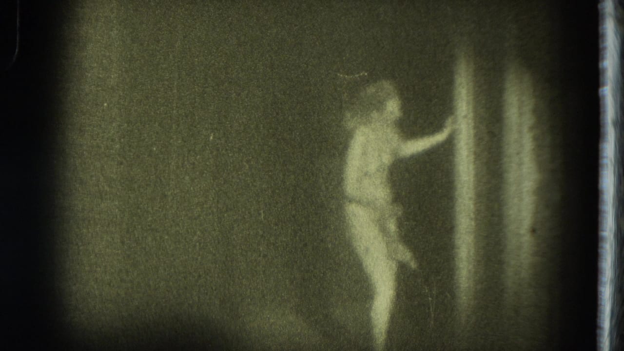 The San Francisco stage performer reaches toward a curtain or sheer fabric during the grainy 1975 8mm burlesque scene.
