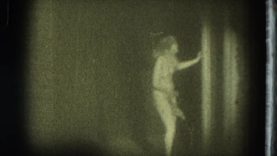 The San Francisco stage performer reaches toward a curtain or sheer fabric during the grainy 1975 8mm burlesque scene.
