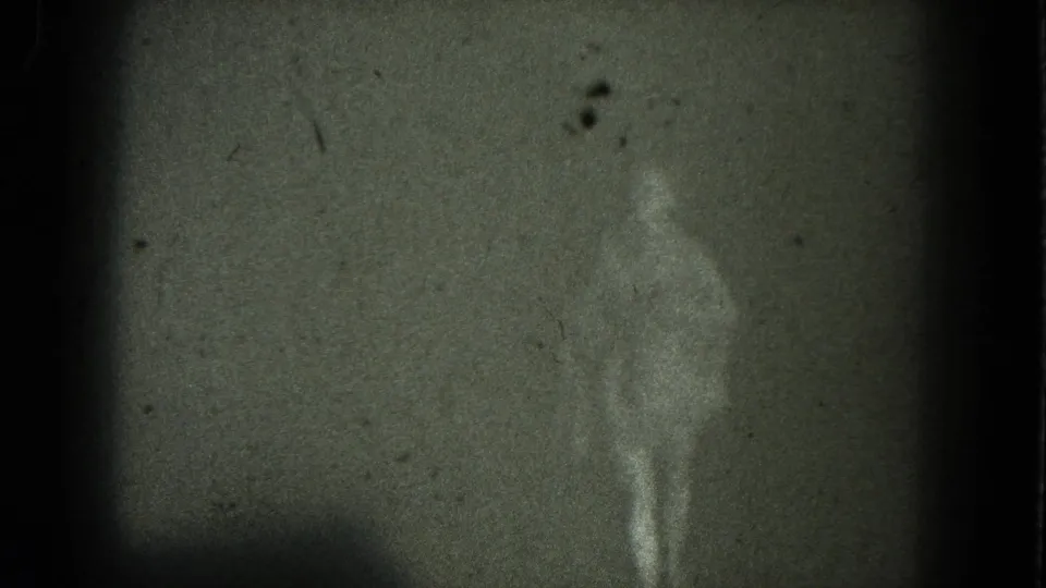 A grainy 1975 San Francisco 8mm frame shows the nude performer standing near dark curtains at the end of the brief stage scene.