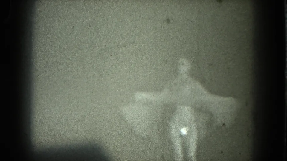 1975 8mm San Francisco home-movie frame of a woman in a pale dress posed with arms outstretched in soft silhouette.