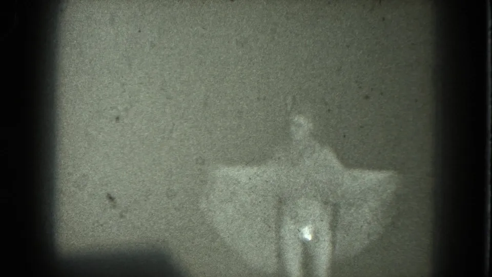 1975 8mm San Francisco frame showing a woman in a pale dress turning or posing with one arm extended.