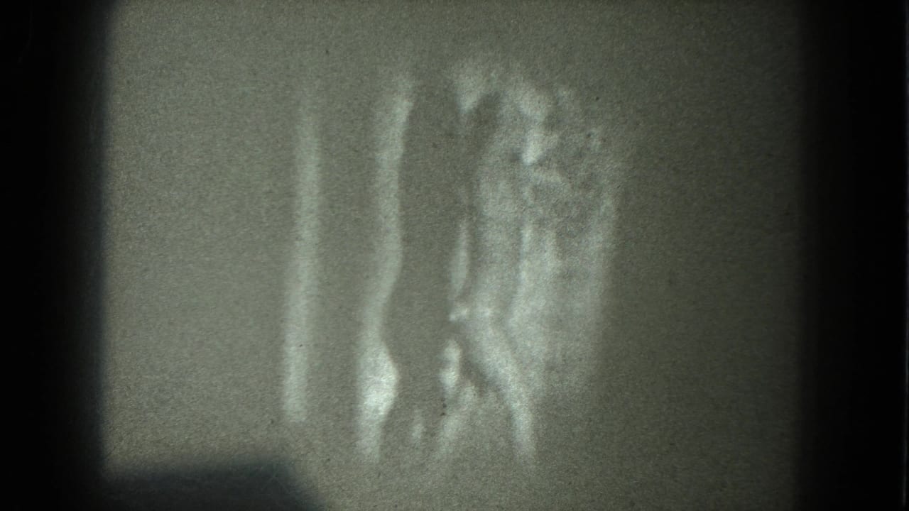 1975 San Francisco 8mm frame showing an adult woman in revealing reflective clothing with arms lifted in a dance pose.