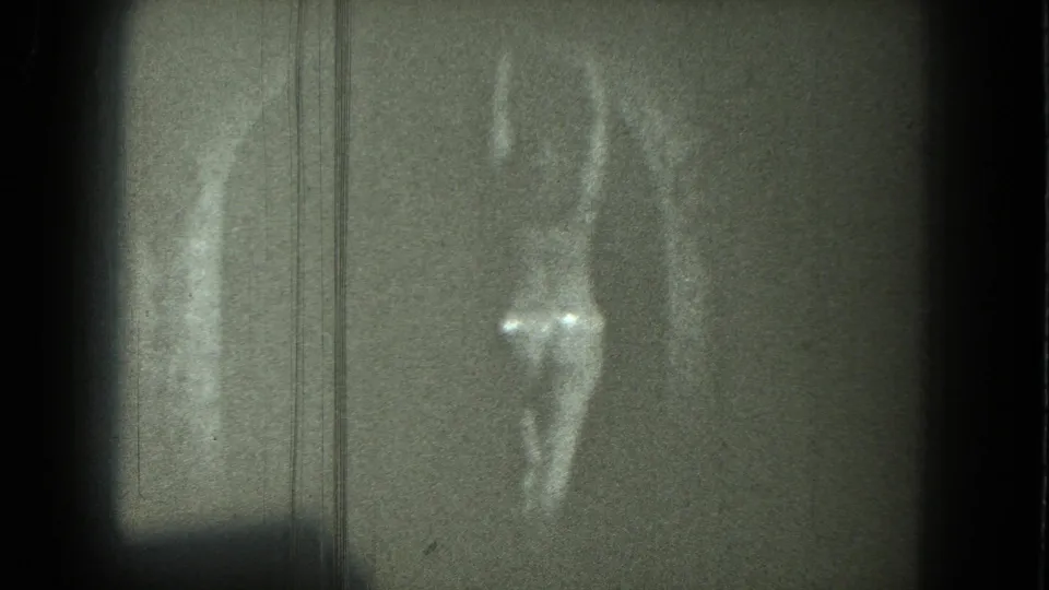 Grainy 1975 San Francisco 8mm frame of an adult woman dancing, with a bright reflective garment visible at the lower body.