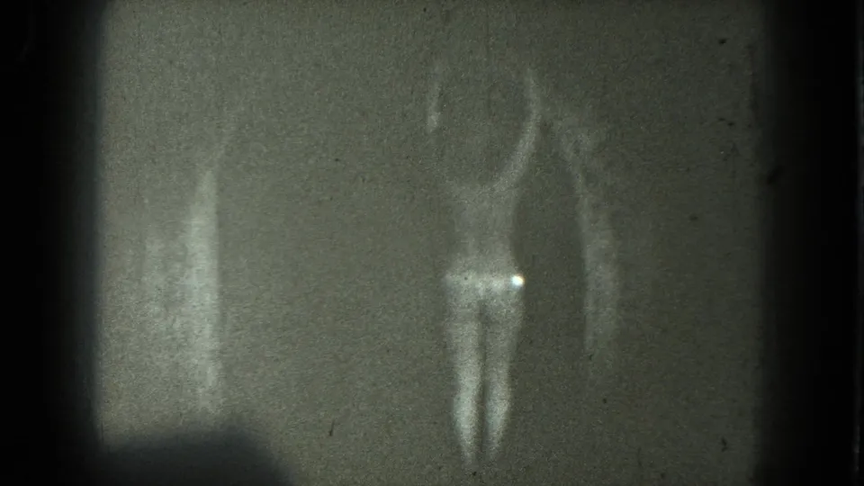 1975 San Francisco 8mm frame of an adult dancer in profile, partly obscured by grain, scratches, and low exposure.