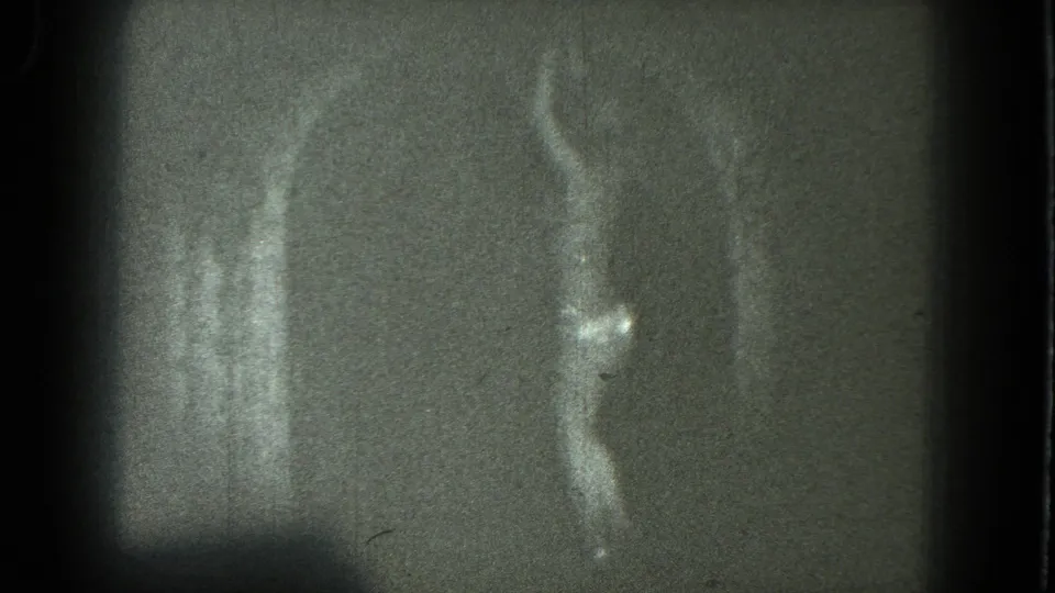 1975 San Francisco 8mm frame showing an indistinct adult dancer near vertical light streaks, with grain and flare prominent.