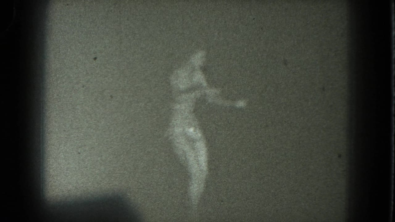 Soft, grainy frame of a woman dancing against a plain dim background.