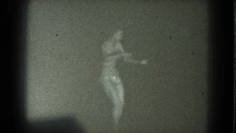 1975 San Francisco 8mm frame showing a woman dancing in soft focus against a plain, dim backdrop.