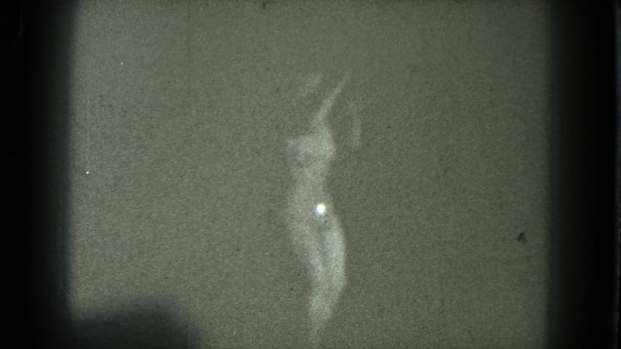 1975 San Francisco 8mm frame of a woman dancing, with one arm raised and a bright highlight on her lower torso.