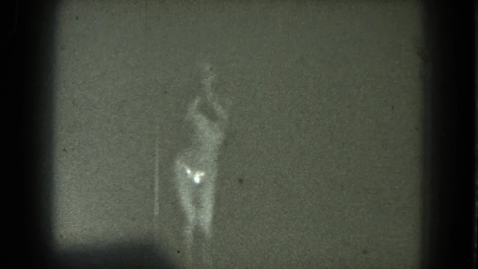 1975 San Francisco 8mm frame of a woman dancing near center, softened by grain, dim exposure, and vertical scratch marks.
