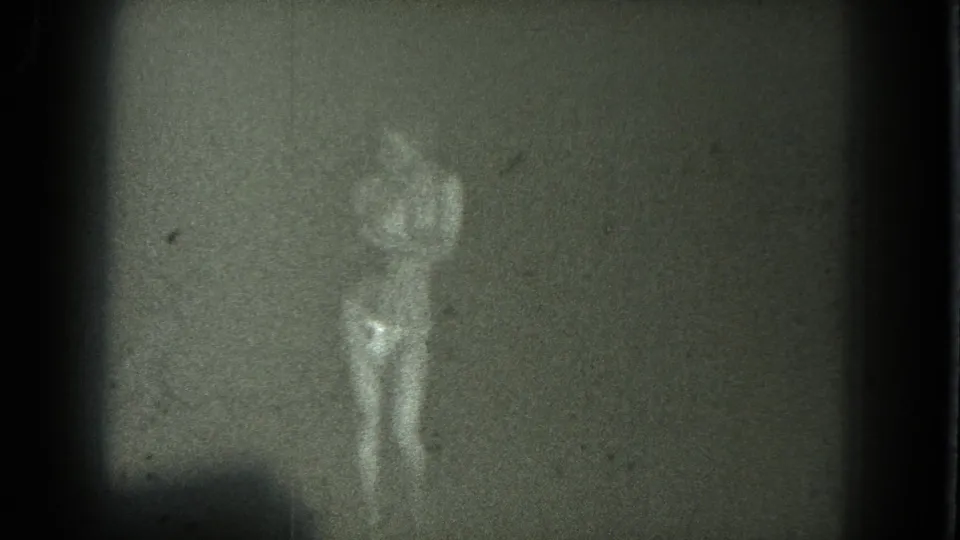 The faint figure of the dancer is visible in a low-light 8mm frame, with one arm raised and details obscured by grain.