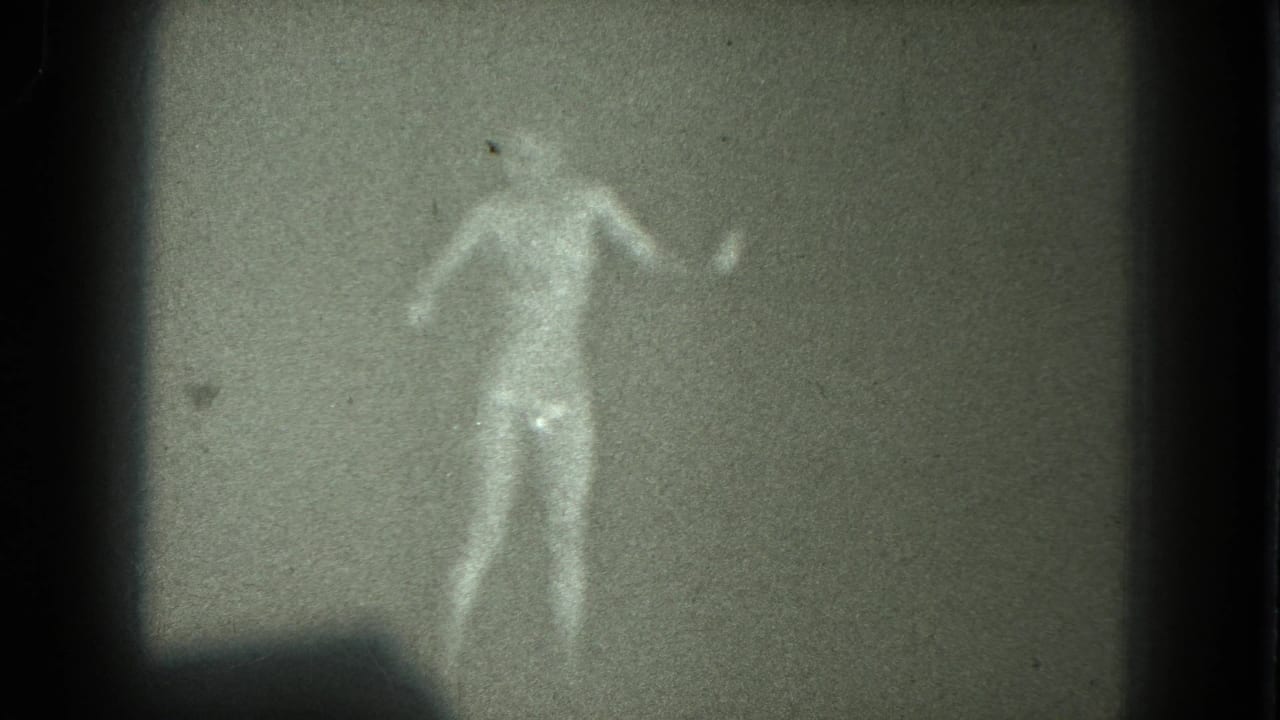 Grainy 1975 8mm frame of a nude adult figure dancing in a dim interior, location supported as San Francisco by metadata.