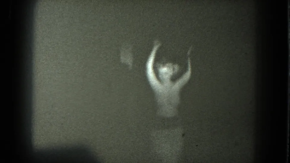 Grainy 1975 8mm frame shows a nude adult dancer low in the composition with arms raised, from San Francisco metadata.