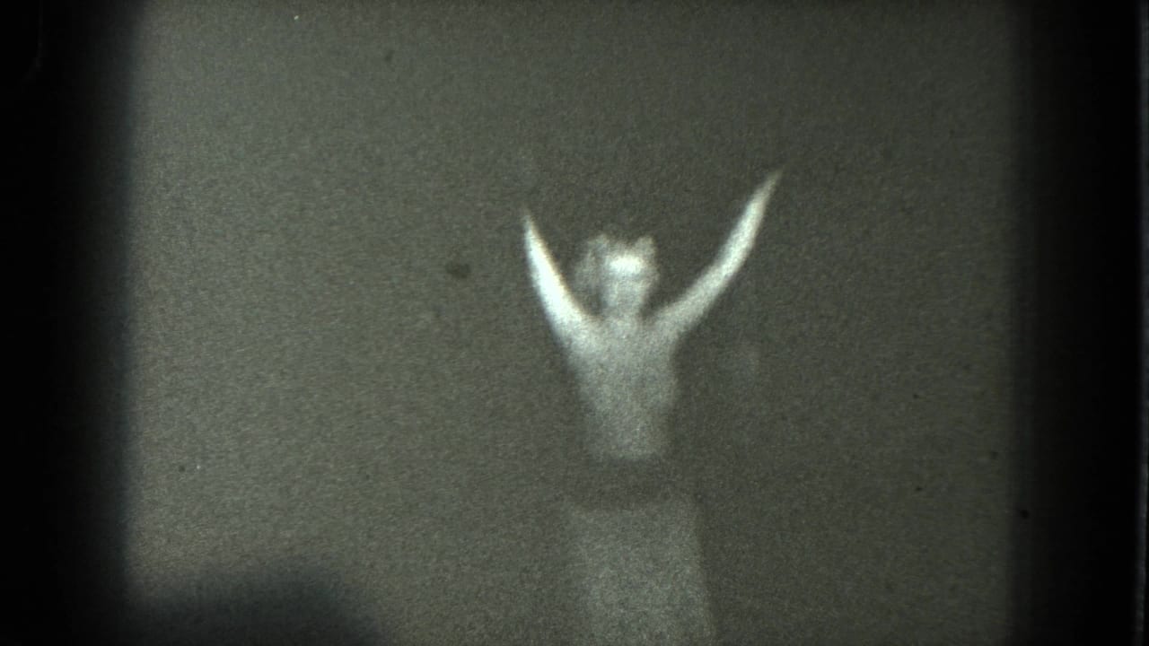 Adult woman performing on a dim San Francisco stage in 1975, seen through grainy 8mm footage with arms lifted.