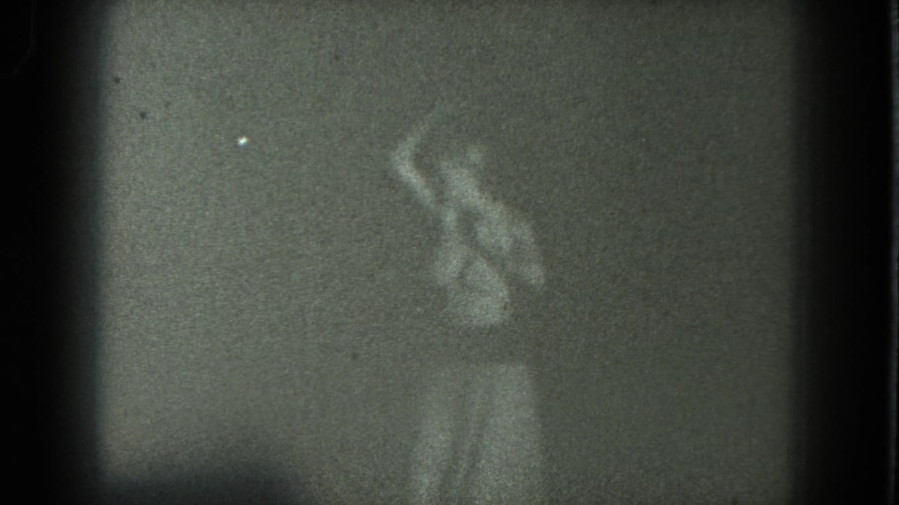 Grainy 1975 8mm view of an adult woman swaying on a dark San Francisco stage near curtains.
