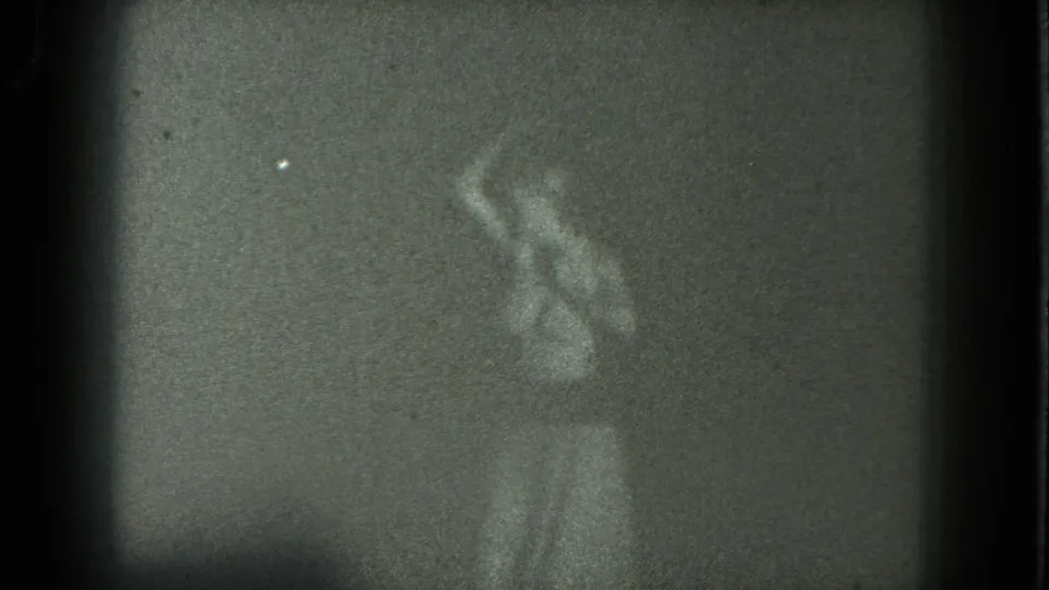 Grainy 1975 8mm view of an adult woman swaying on a dark San Francisco stage near curtains.