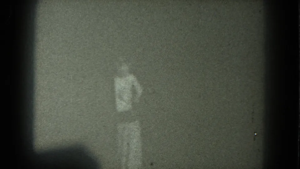Grainy 1975 San Francisco 8mm frame of an adult figure standing in low light after the raised-arm pose.