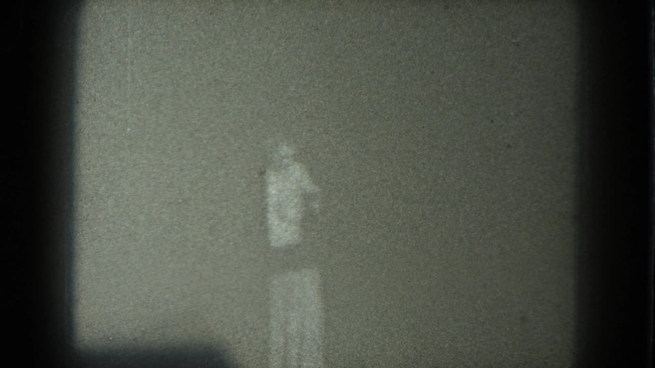 Faint person standing near a dark corner in a grainy low-light frame.