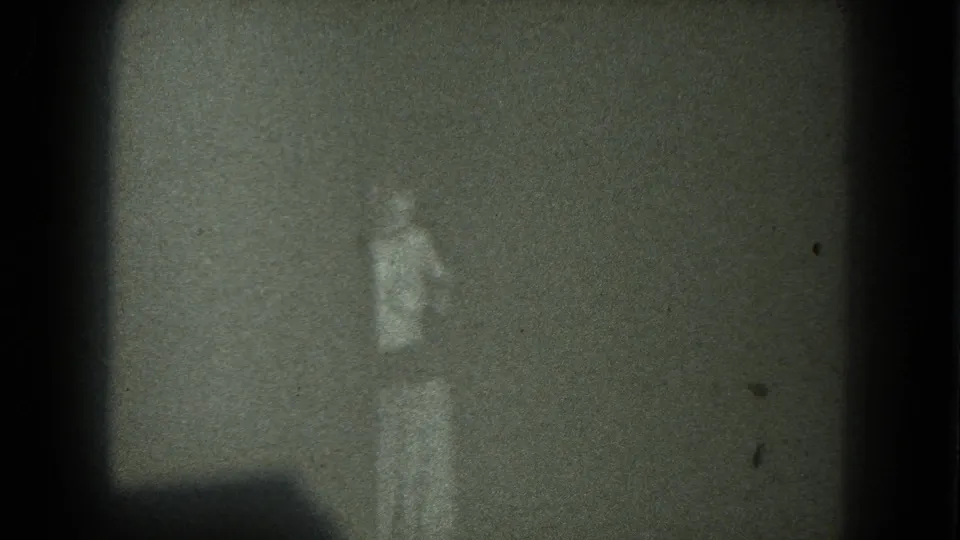Low-light 8mm frame showing a faint person in light clothing near a shadowed corner, San Francisco metadata supported.