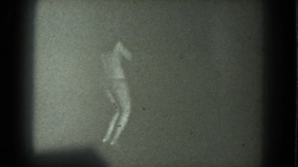 Dim 1975 home-movie frame of an adult woman bending slightly as she dances alone in bikini and heels.