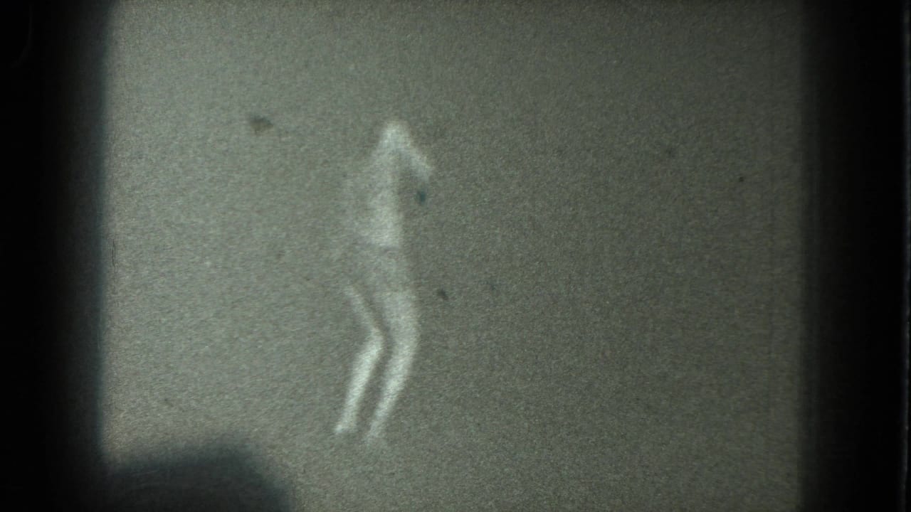 A low-light 1975 San Francisco 8mm frame shows a dancer silhouette with legs visible against a dark, grainy backdrop.
