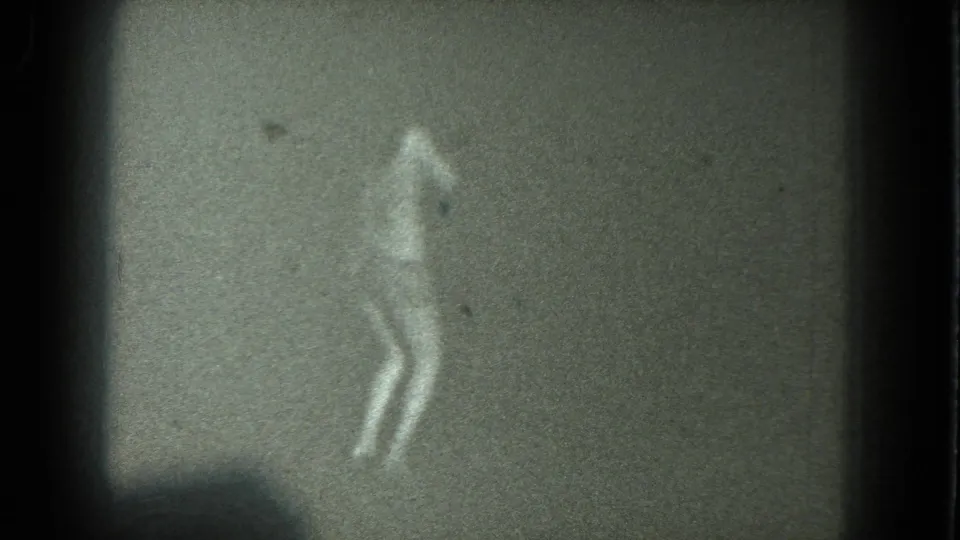 A low-light 1975 San Francisco 8mm frame shows a dancer silhouette with legs visible against a dark, grainy backdrop.