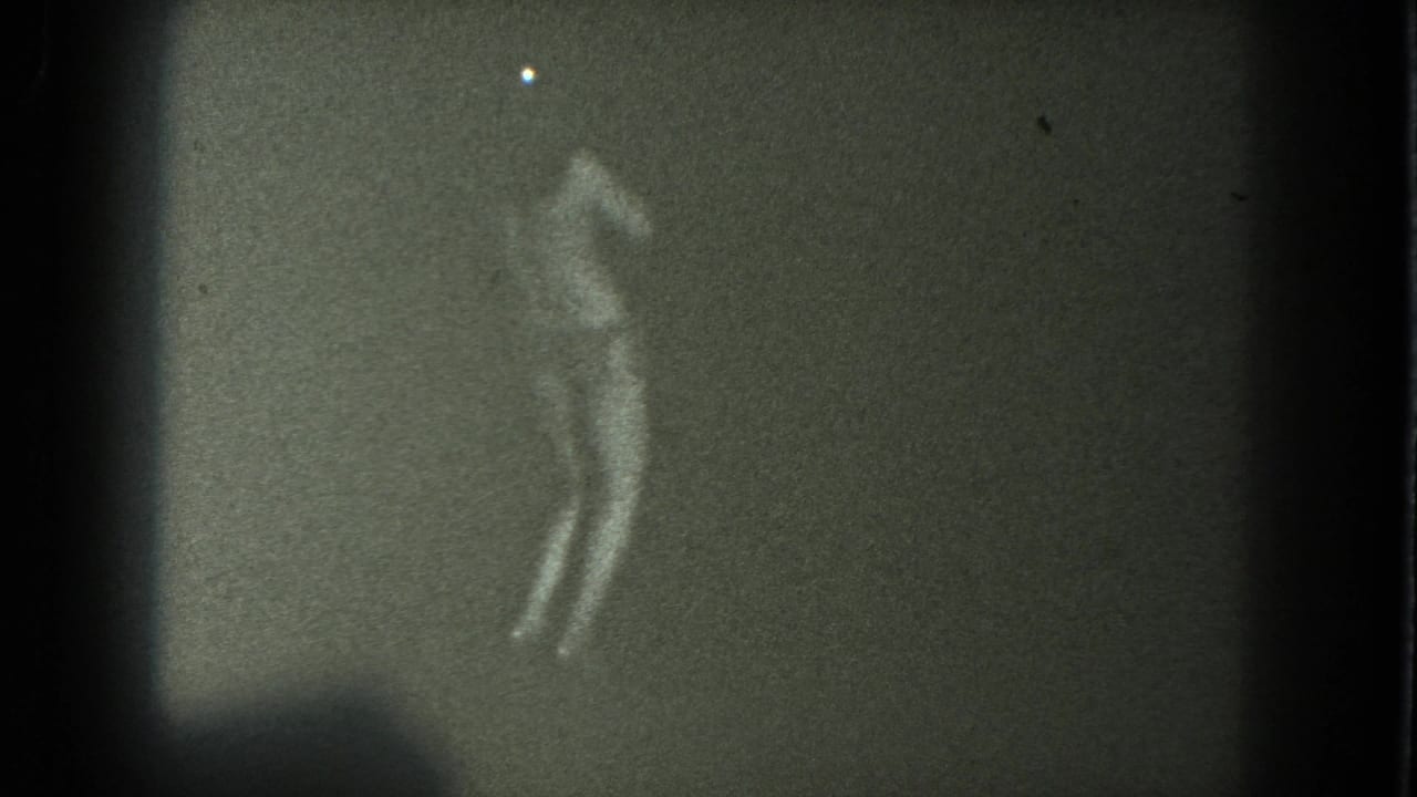 A silhouetted performer appears to lean or sway with one arm raised in a grainy 8mm frame from the San Francisco clip.