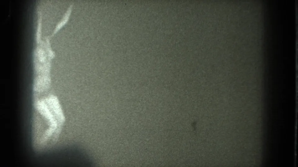 A low-light 8mm frame shows the performer partly cut off at left, one arm raised and legs bent during movement.