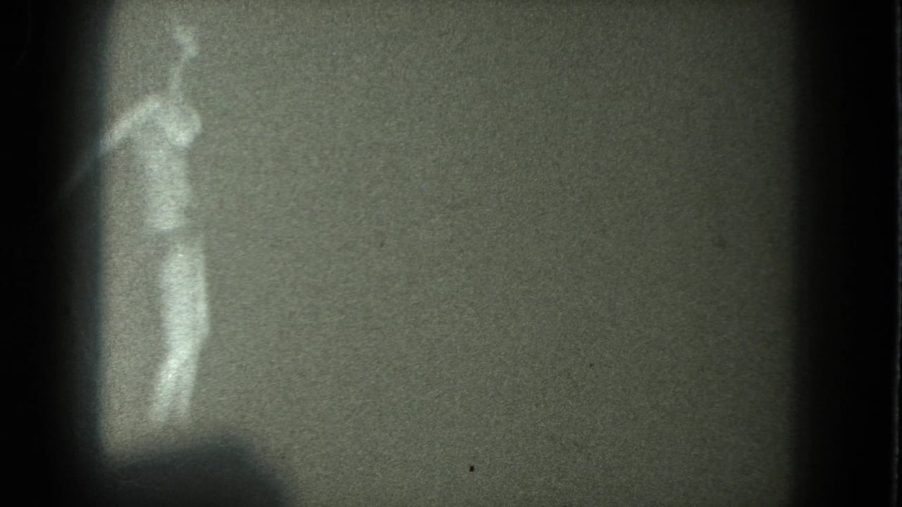 1975 San Francisco 8mm frame showing a woman in minimal clothing or nude, blurred by grain and high contrast as she dances near the left edge.