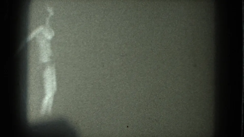 1975 San Francisco 8mm frame showing a woman in minimal clothing or nude, blurred by grain and high contrast as she dances near the left edge.