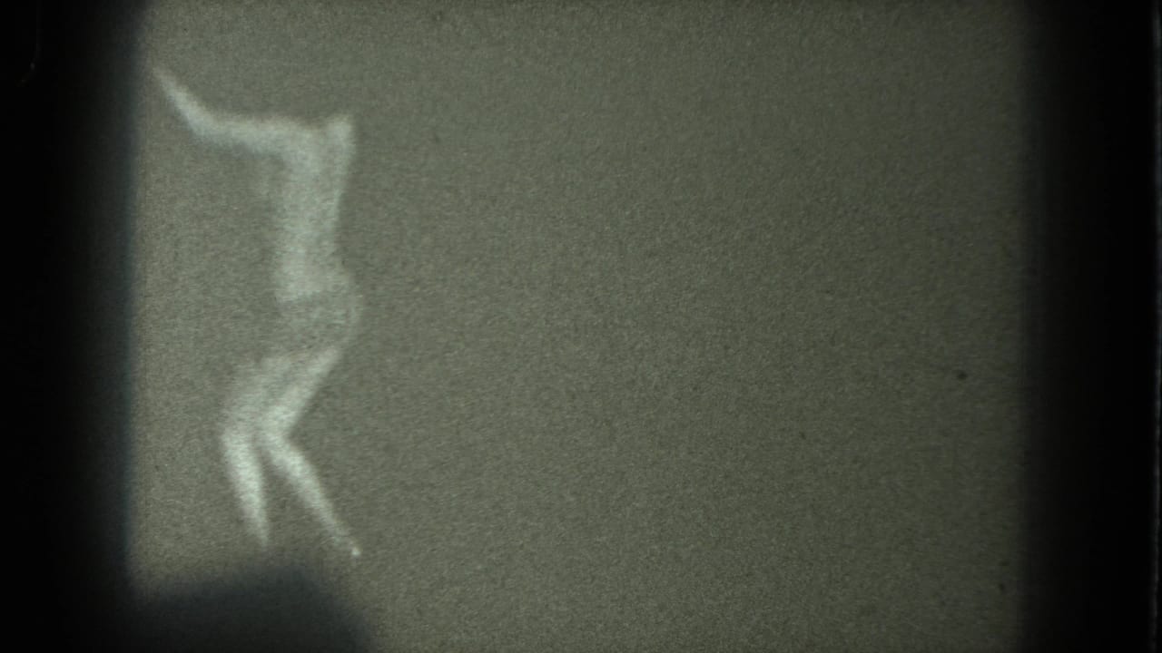 Blurred black-and-white frame of a woman bending or turning while dancing against a plain dark background.
