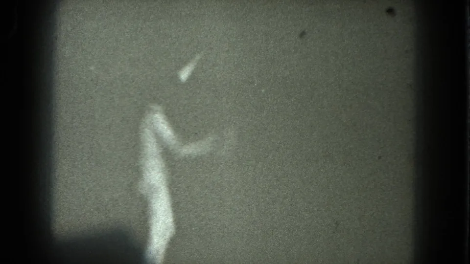 1975 8mm San Francisco footage showing a soft, shadowy female dancer near a plain wall, framed by dark film edges.