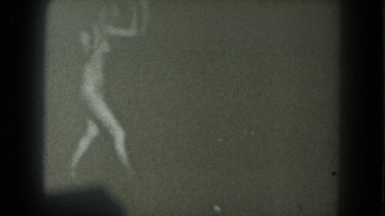 A blurred adult woman appears to dance in a dark, grainy 1975 8mm home-movie frame from San Francisco metadata.