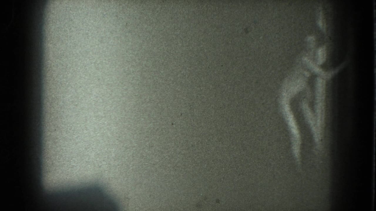 The figure stands near the right side of the 8mm frame, softened by low light, film grain, and motion blur.