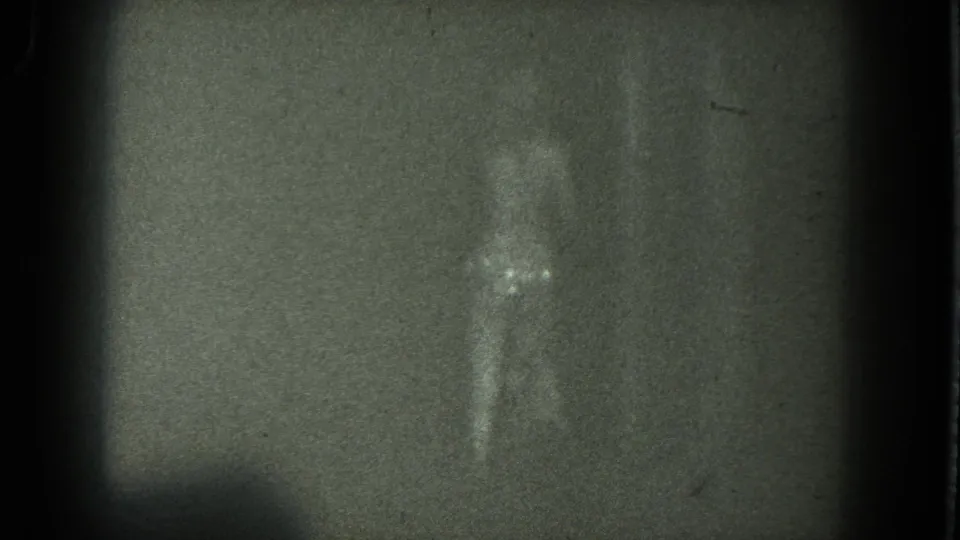 1975 San Francisco 8mm frame of a woman dancing in a dark room, with one arm lifted and her figure partly blurred by motion.